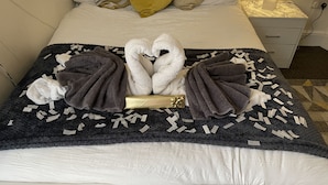 A neatly made bed with a towel arrangement in the center, a bedside table with a lamp, and a patterned rug on the floor. - Hidden Hot Tub Retreat Apartment in Nottingham (Nottingham)