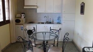 A compact kitchen with a glass table and four chairs, a microwave, a kettle, and a water dispenser. - Rustic 1-bed Bungalow in Parque Holandés (La Oliva)