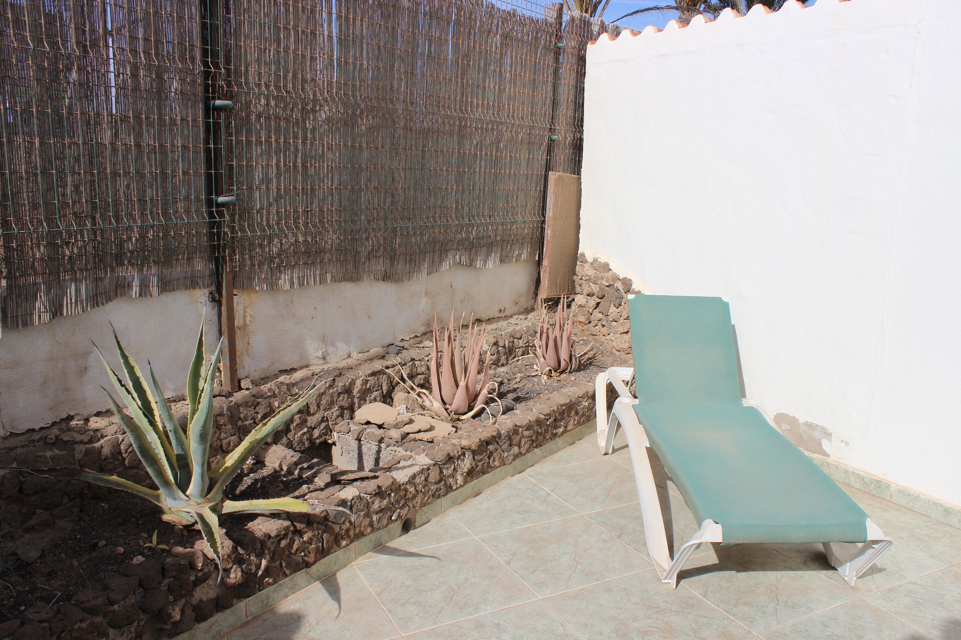 A small outdoor area with a white wall, a metal fence, and a green lounge chair.