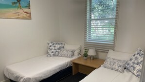Une chambre avec deux lits simples, une petite table avec une lampe et une fenêtre avec des stores.
