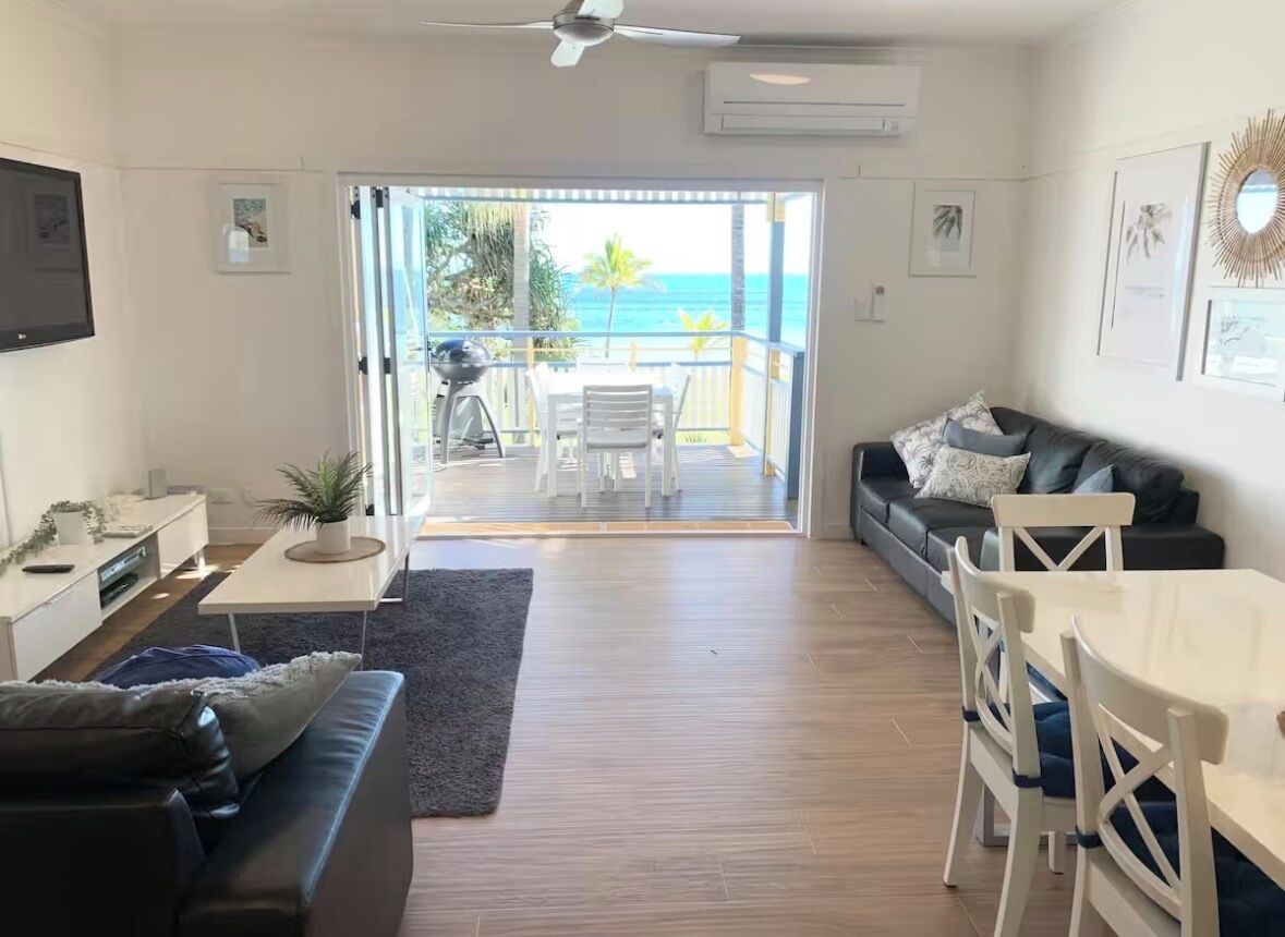 Un salon comprenant un canapé, une table à manger avec des chaises, un ventilateur de plafond et une vue sur l’océan par une porte-fenêtre coulissante.