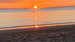 Une scène de plage avec un coucher de soleil sur l’eau, un bateau et une côte lointaine.