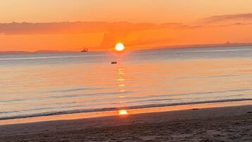 A beach scene with a sunset over the water, a boat, and a distant shoreline.