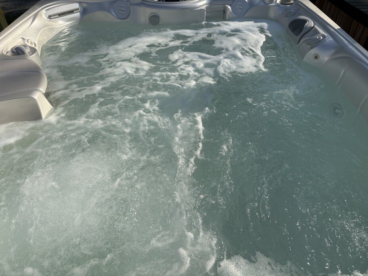 A hot tub with visible bubbles and water movement, surrounded by a wooden deck.