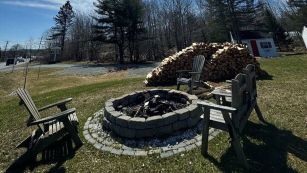 A backyard with a fire pit, two Adirondack chairs, and a stack of firewood. - 16 Apartment near Acadia Open Hearth Inn (Trenton)