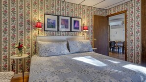 A bedroom with floral wallpaper, a bed with floral bedding, two framed pictures on the wall, and a small table with a vase of flowers. - 16 Apartment near Acadia Open Hearth Inn (Trenton)