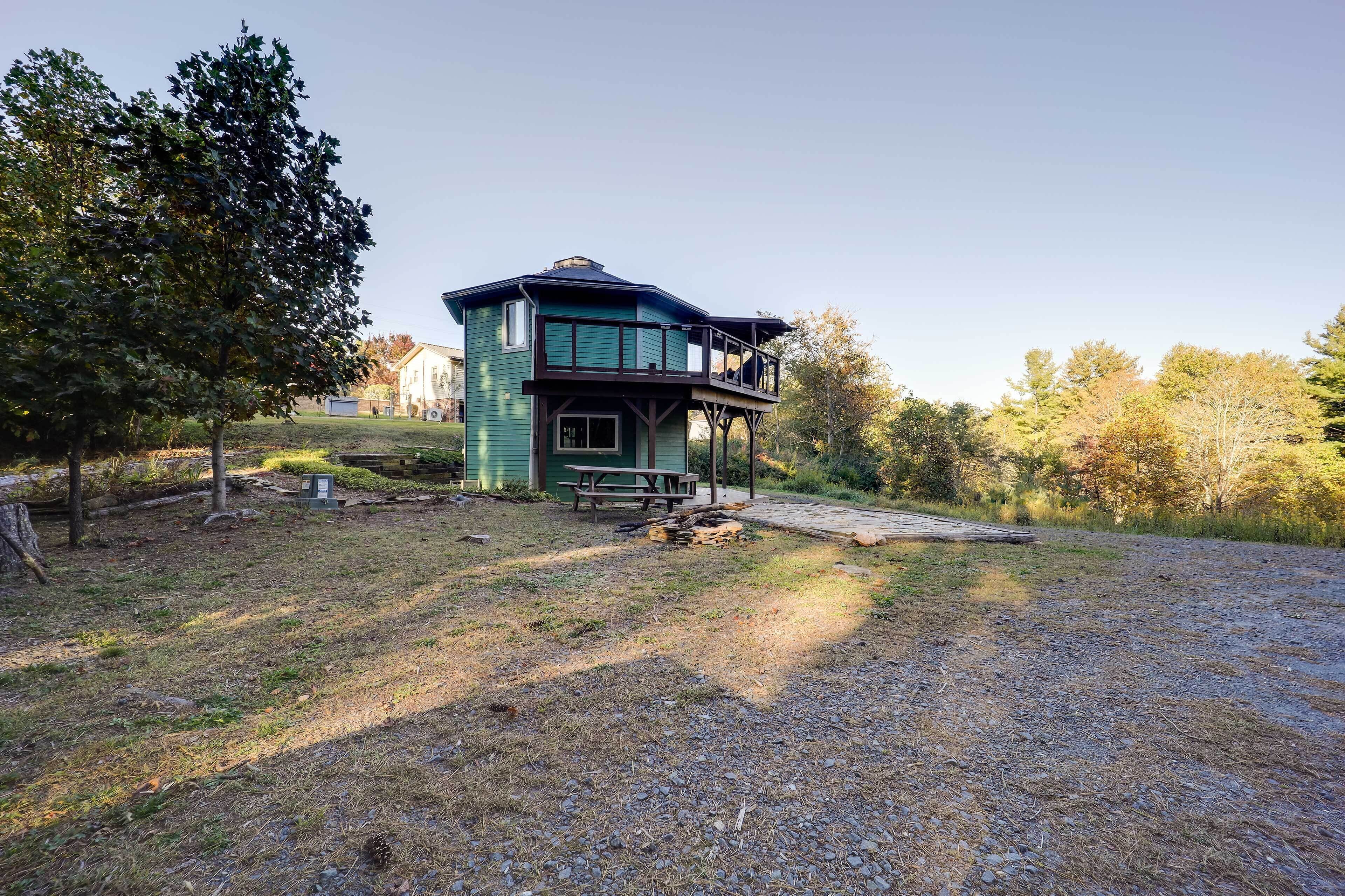 Une maison à deux étages avec un balcon, entourée d’arbres et donnant sur une allée gravillonnée.