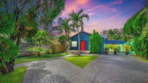 Ein modernes Haus mit roter Tür, umgeben von üppiger Vegetation und einem gepflasterten Einfahrt.