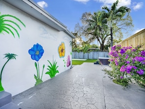 Stroll through a serene garden oasis with a paved walkway, vibrant mural, and lush greenery.
