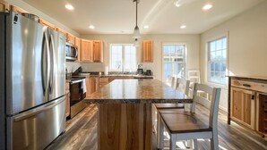 A modern kitchen with a large island, stainless steel appliances, wooden cabinets, and ample natural light. - Newly Built Lake Front Home (Lake Pleasant)
