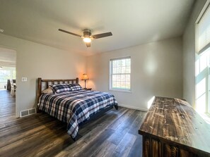 A bedroom with a bed, a nightstand, a lamp, a ceiling fan, and a window. - Newly Built Lake Front Home (Lake Pleasant)