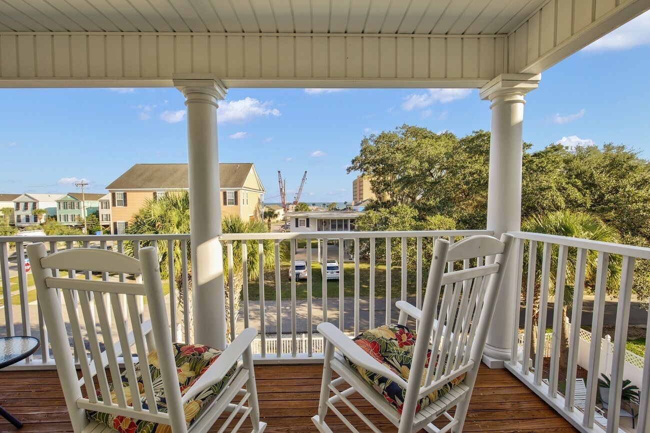 A covered porch with white railings and two rocking chairs with floral cushions.