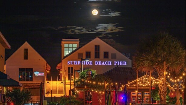 Una proprietà fronte spiaggia chiamata 'Surfside Beach Pier', con un cartello, un edificio con un'ampia vetrata e luci decorative.
