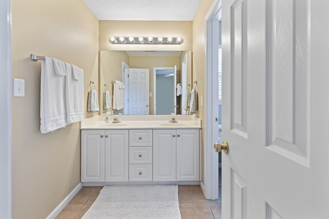 A bathroom with white cabinets, a large mirror, and a vanity with a lighted vanity mirror.