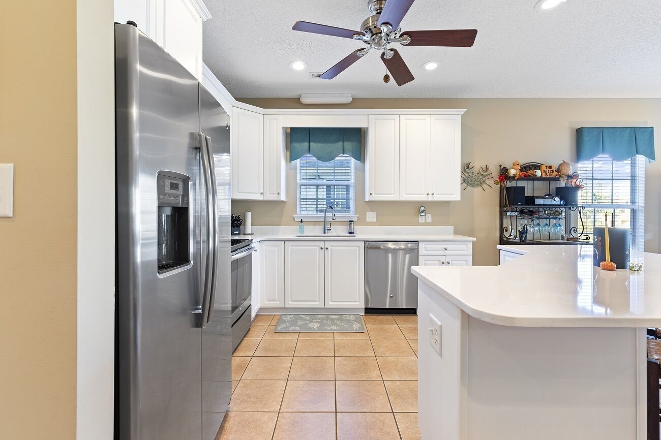 A modern kitchen with white cabinets, stainless steel appliances, a central island, and a ceiling fan.