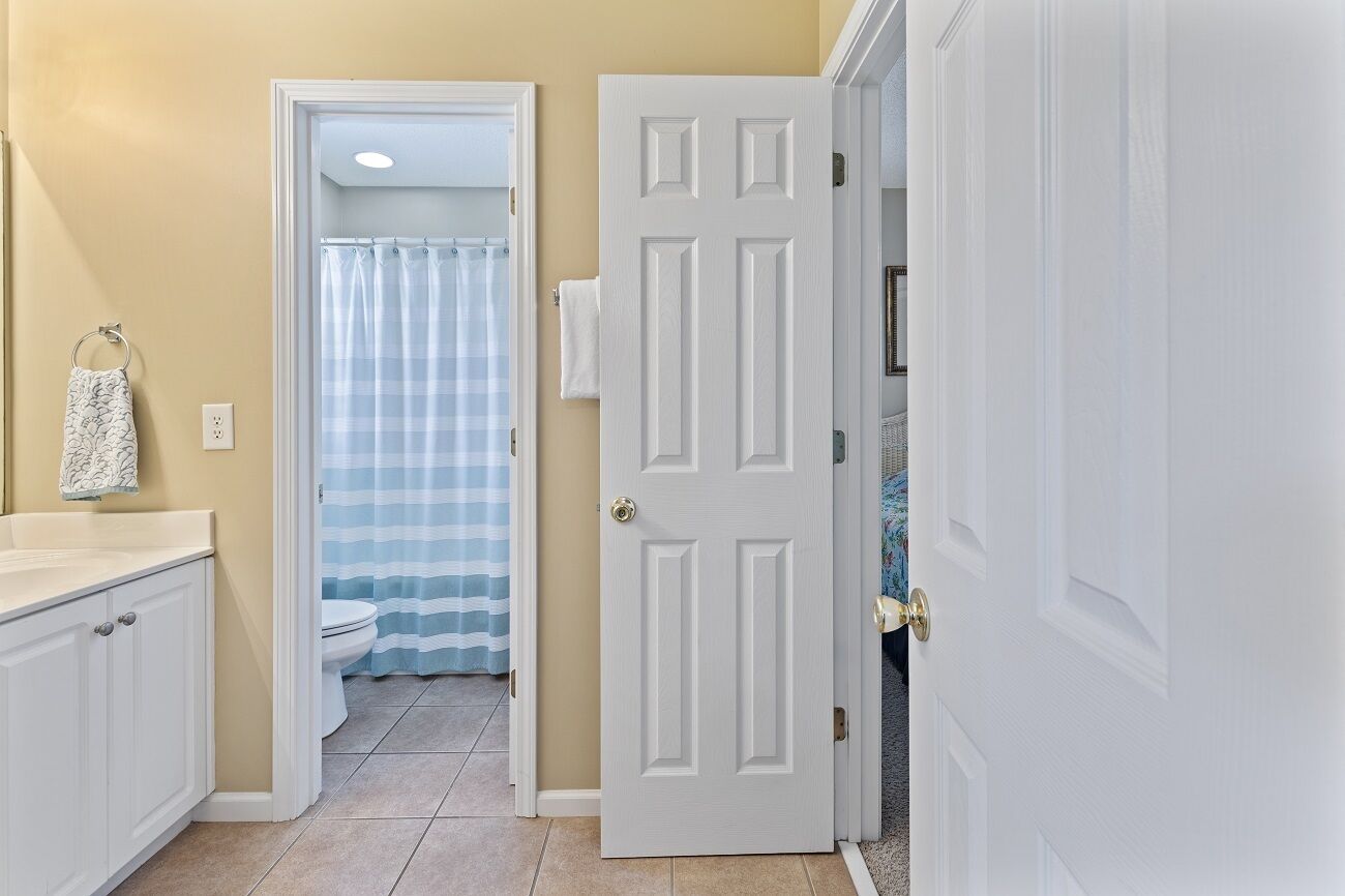 A hallway with a white door, a bathroom with a striped shower curtain, and a white towel hanging on a rack.