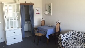 A compact living space with a dining area, a sofa, a cabinet with glass doors, and a small table. - Helene - Sylt - Relaxed island life: Cozy vacation apartment in Westerland (Sylt)