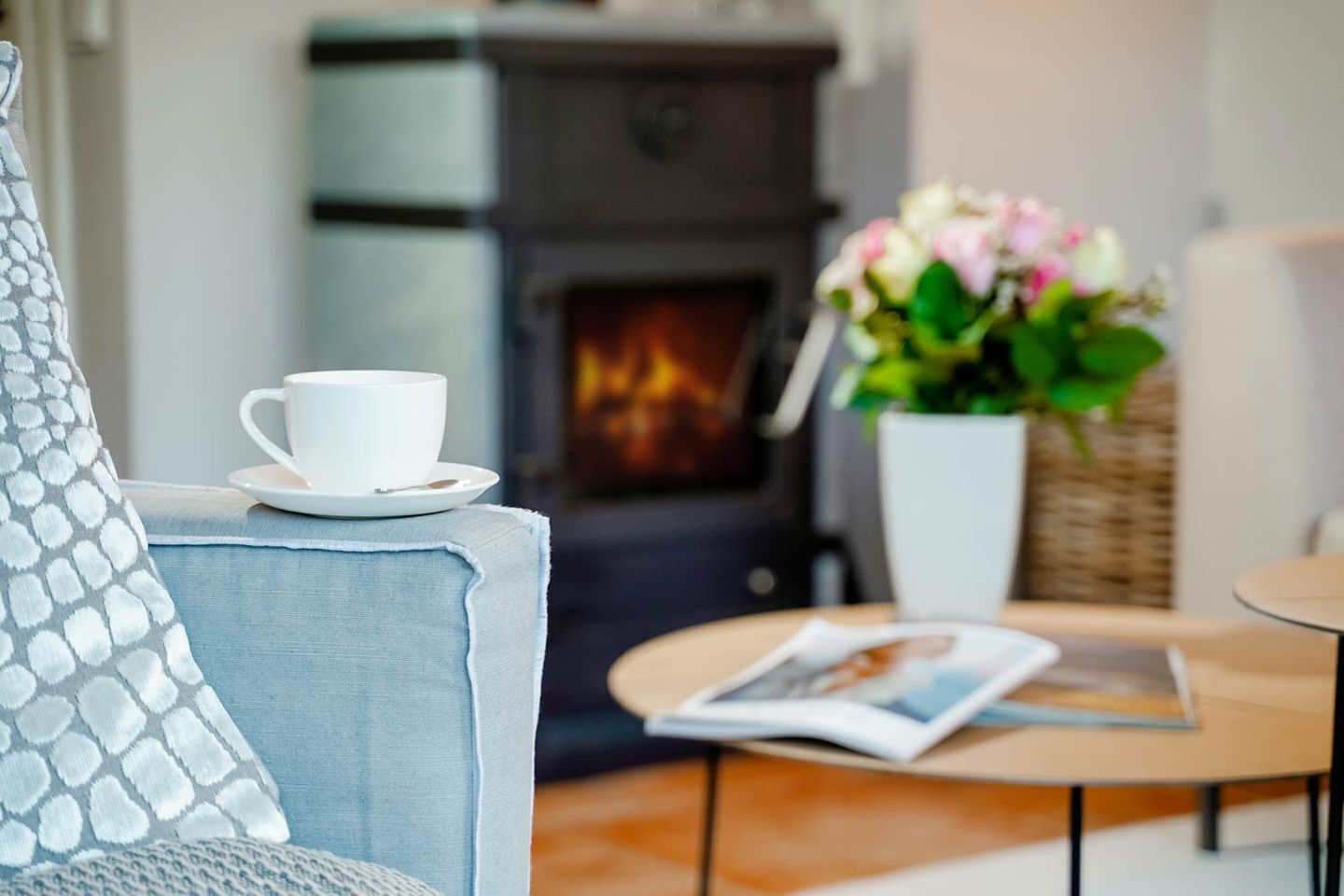 A cozy living room with a fireplace, a white cup on a side table, and a magazine.