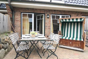 Eine Terrasse mit Tisch für zwei Personen, umgeben von Metallstühlen und einer Sitzgelegenheit im Freien mit Streifenmuster.