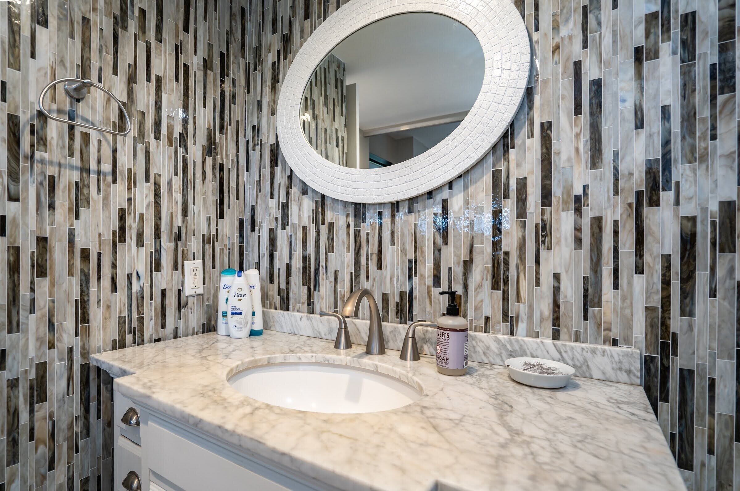 A bathroom with a marble sink, a round mirror, and toiletries on the counter.
