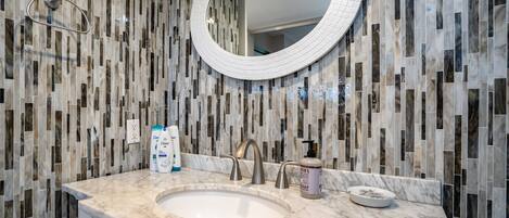 A bathroom with a marble sink, a round mirror, and toiletries on the counter.