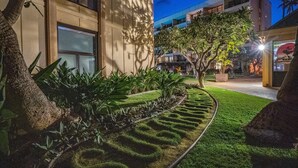 A landscaped garden with a curved pathway, a tree, and a building in the background.