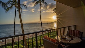 A balcony with a view of the ocean and palm trees at sunset.