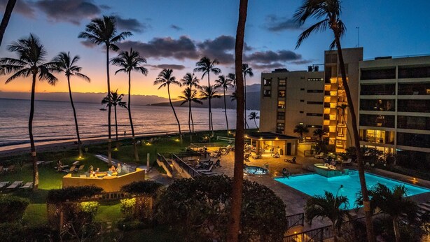 A resort with a pool, outdoor seating, and palm trees.