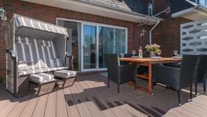 A patio with a wooden table, black wicker chairs, and a cushioned seating area with striped cushions. - Blaue Huis ground floor with sauna - Welcome to the "Blaue Huis" (Sylt)