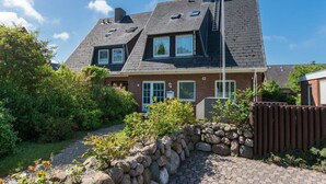 A two-story house with a sloped roof, a stone wall in front, and a flag on a pole. - Blaue Huis ground floor with sauna - Welcome to the "Blaue Huis" (Sylt)