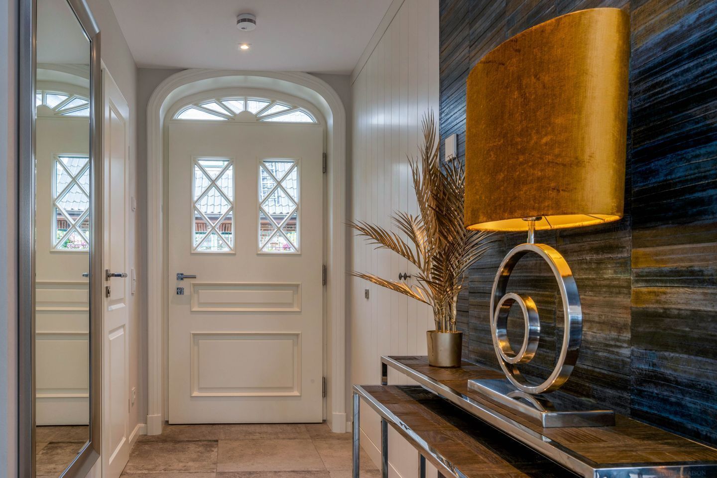 A hallway with a white door, a potted plant, and a modern lamp.