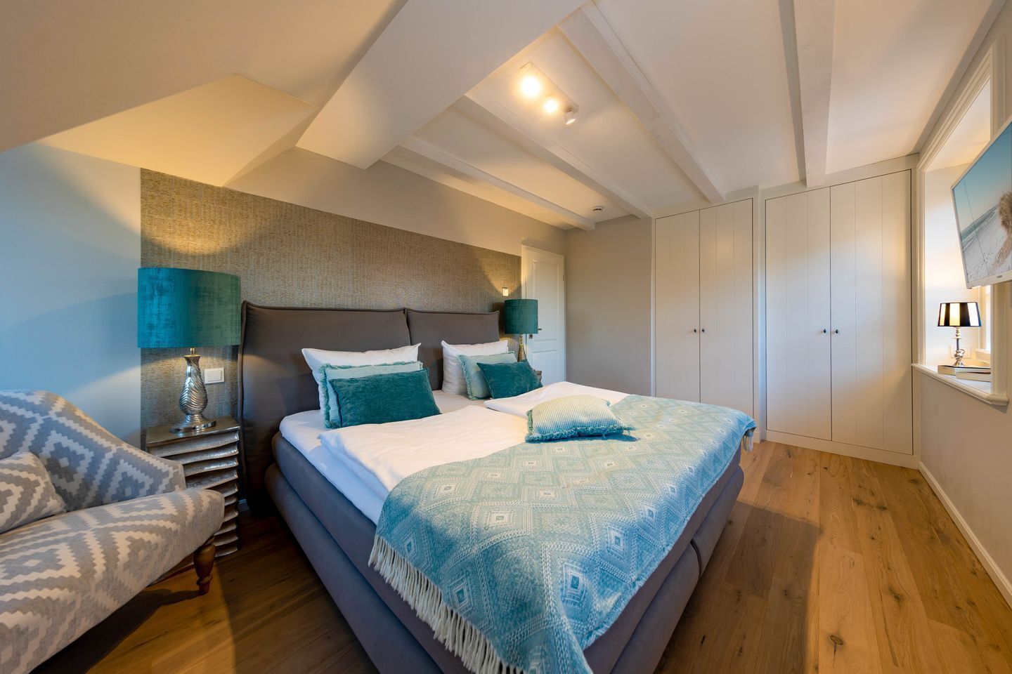 A bedroom with a bed, bedside tables, a chair, and a wardrobe.