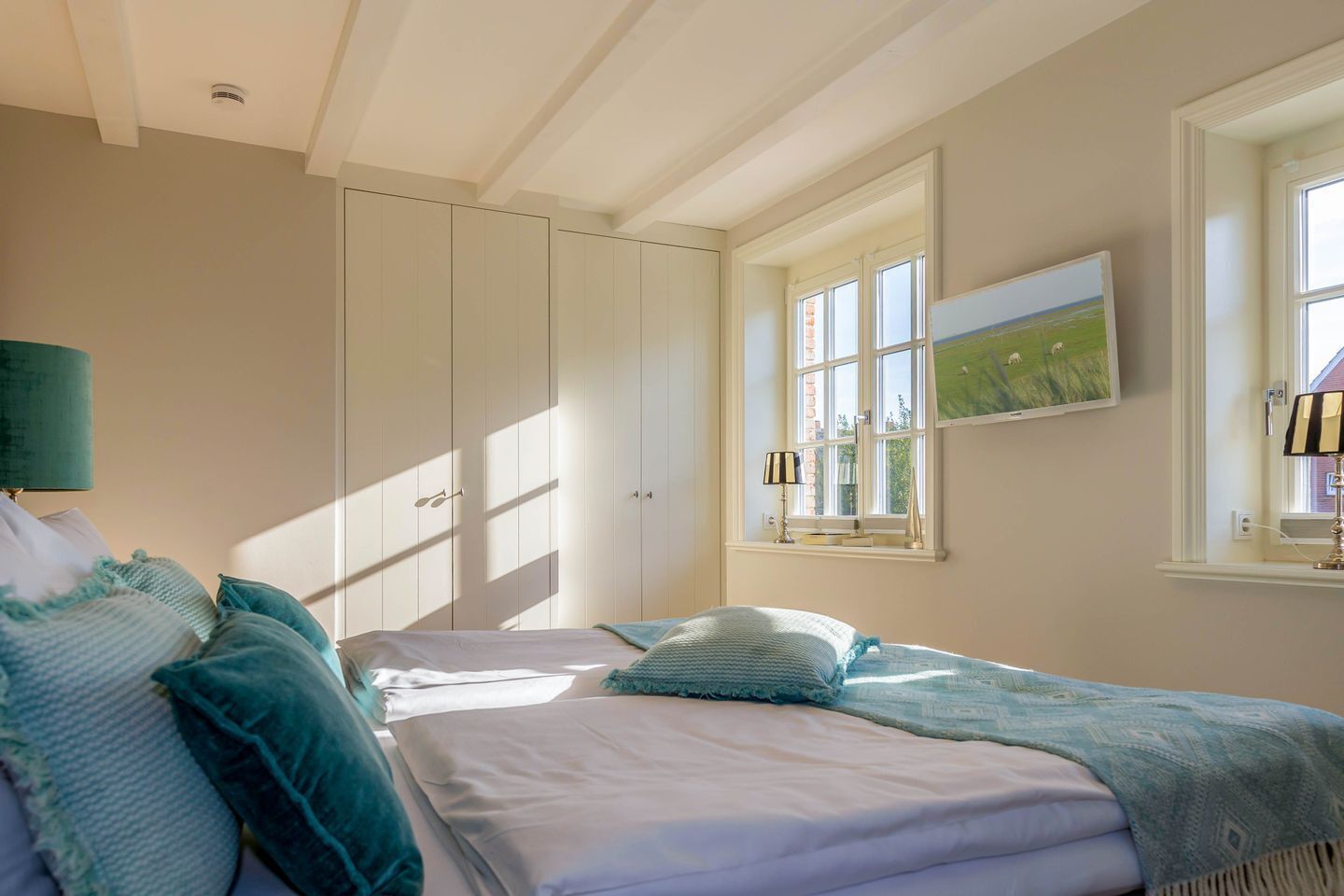 A bedroom with a bed, a wardrobe, a window with a view of a field, and a lamp.