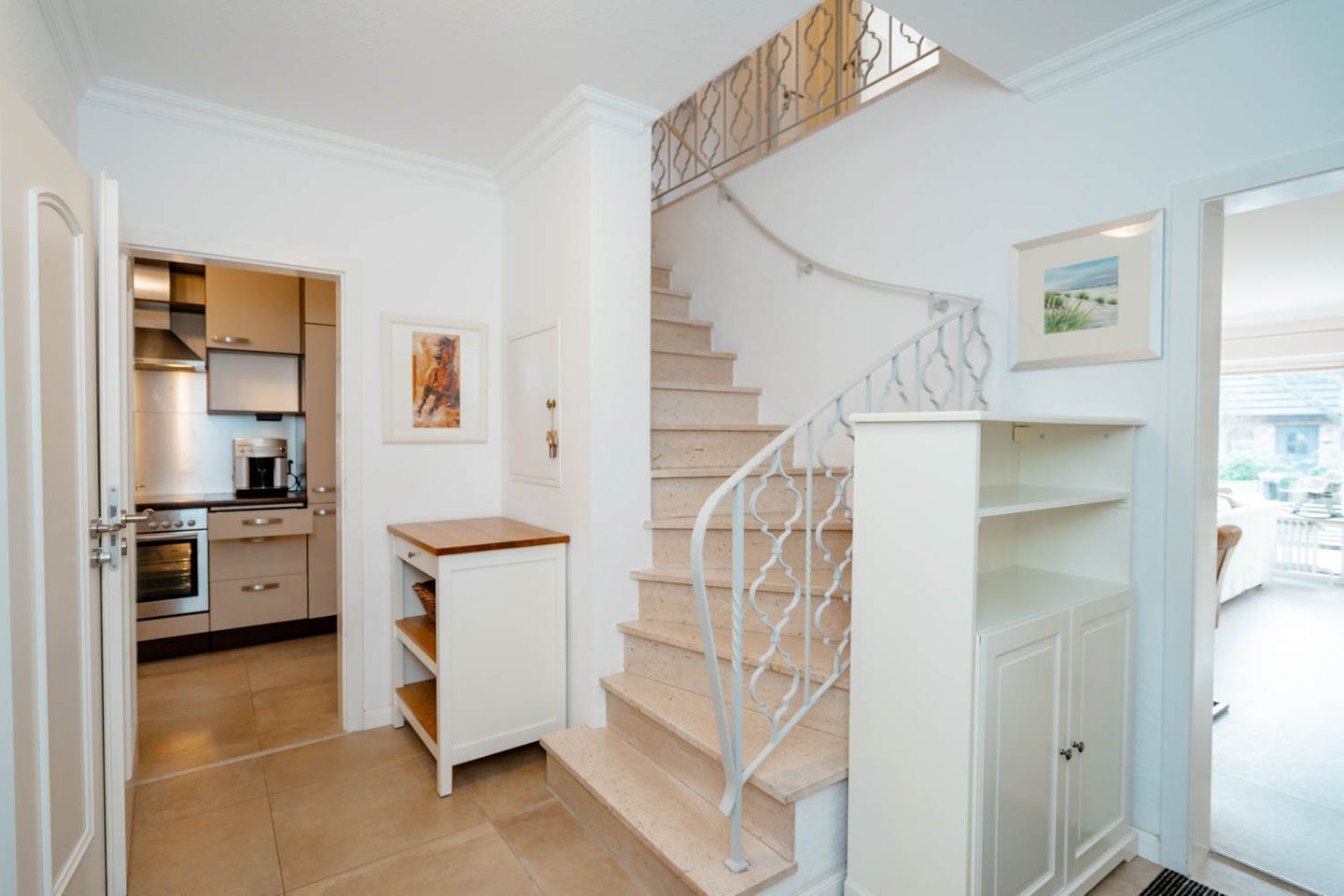 A modern kitchen with built-in appliances, a staircase with decorative railings, and a view of the outside.