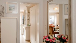 A hallway with a white door, a mirror, and a vase of flowers on a wooden table. - Haus Sprotte - Welcome to the "Sprotte" house (Sylt-Ost)