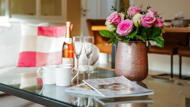 A glass table with a bottle of champagne, two glasses, and a vase of pink roses. - Haus Sprotte - Welcome to the "Sprotte" house (Sylt-Ost)