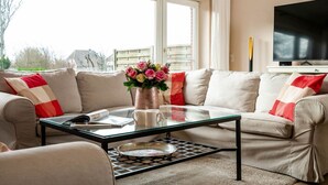 A living room with a beige sofa, a glass coffee table, and a flat-screen TV on a stand. - Haus Sprotte - Welcome to the "Sprotte" house (Sylt-Ost)