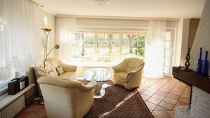 Un salon spacieux comprenant un canapé, deux fauteuils, une table basse et une grande fenêtre donnant sur l’extérieur.