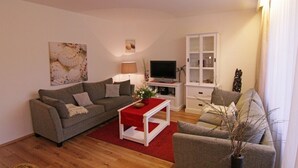 Una sala de estar con un sofá gris, una mesa de centro roja, un televisor y un aparador.