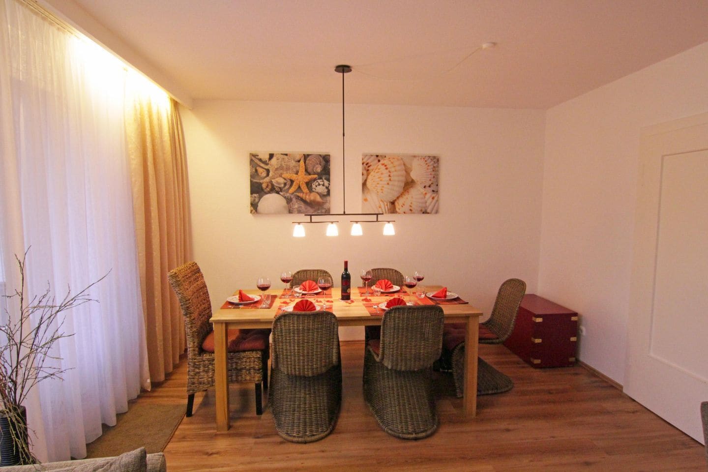 Een eetruimte met een houten tafel voor vier personen, omringd door rieten stoelen. Daarboven hangen twee wandlampen.