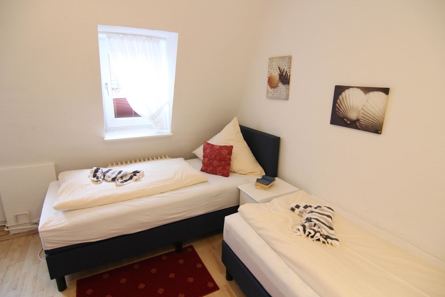 A bedroom with two beds, a window, and wall art.
