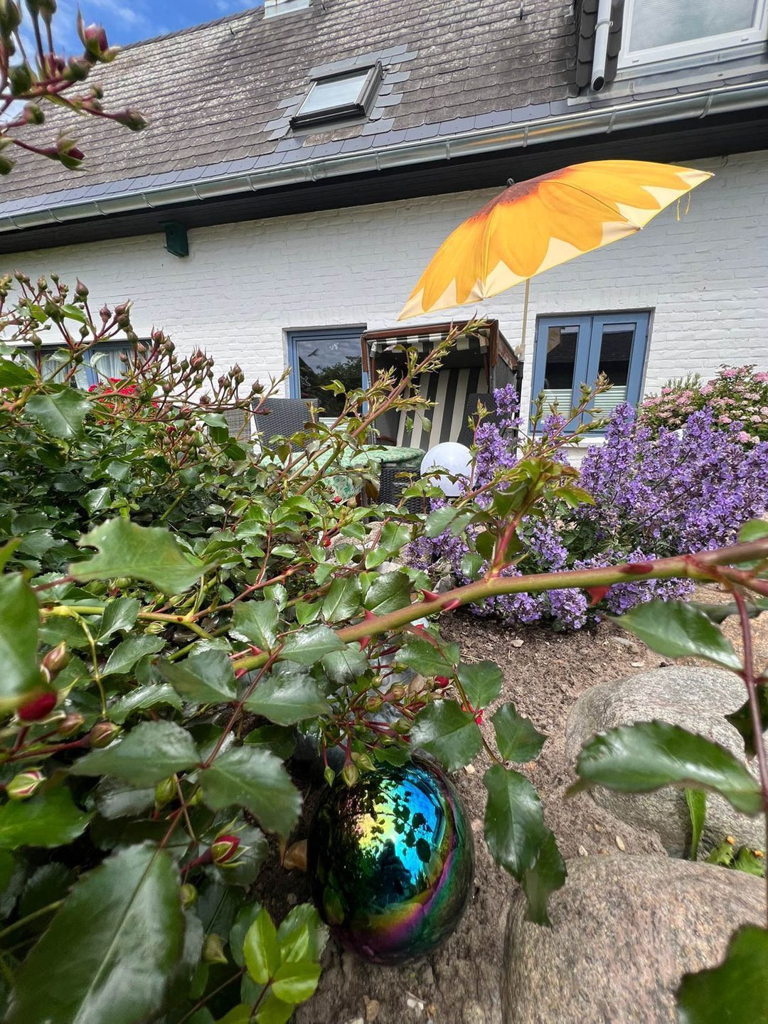A garden with a white building, a large yellow umbrella, and purple flowers.