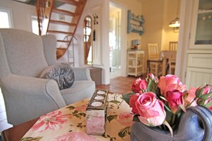 A living room with a grey sofa, a floral tablecloth, a vase of pink roses, and a set of candles.