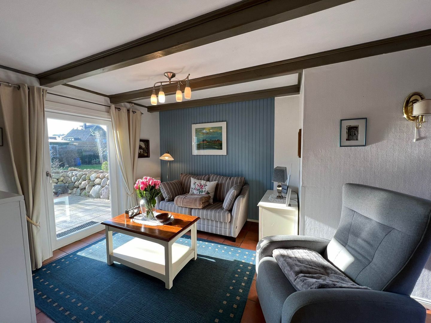 A living room with a sofa, a coffee table, and a lamp. There is a window with curtains and a view of the outside.