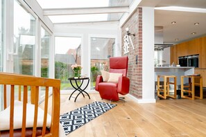 Una sala de estar moderna con un sillón rojo, una mesita con un jarrón de flores y vistas al jardín a través de amplios ventanales.