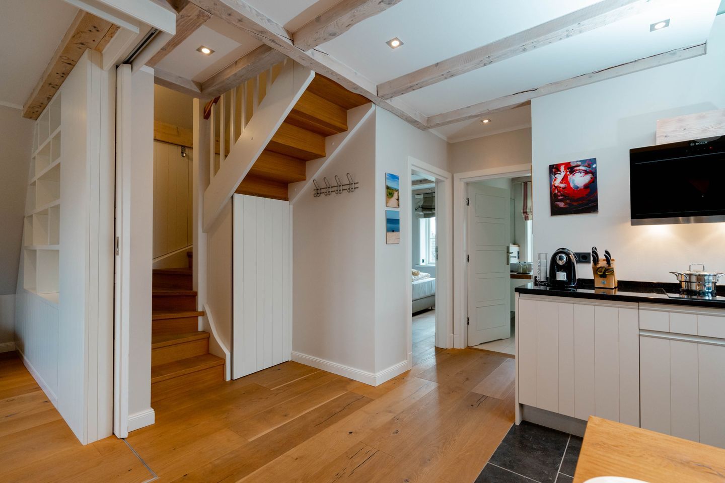 A modern kitchen with white cabinets, a wooden staircase, and a flat-screen TV mounted above the counter.
