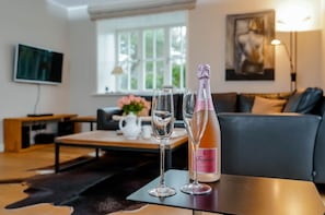 Una sala de estar con un sofá, una mesa de centro con un jarrón de flores y una botella de Freixenet champagne sobre una mesa.