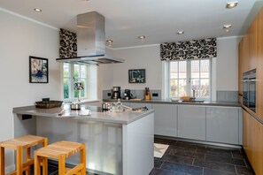 A modern kitchen with a central island, wooden stools, and a large window providing natural light. - Beachfront Lodge on Sylt with Sauna - Welcome to the Luxury Vacation Home (Sylt)