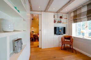 A modern kitchen with white cabinetry, a wooden dining table, and a TV mounted above it. - Beachfront Lodge on Sylt with Sauna - Welcome to the Luxury Vacation Home (Sylt)