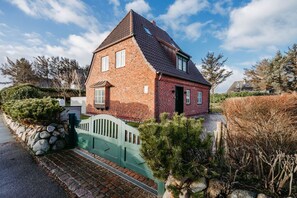 A red brick house with a steep gabled roof, a green gate, and a stone pathway leading to the entrance.